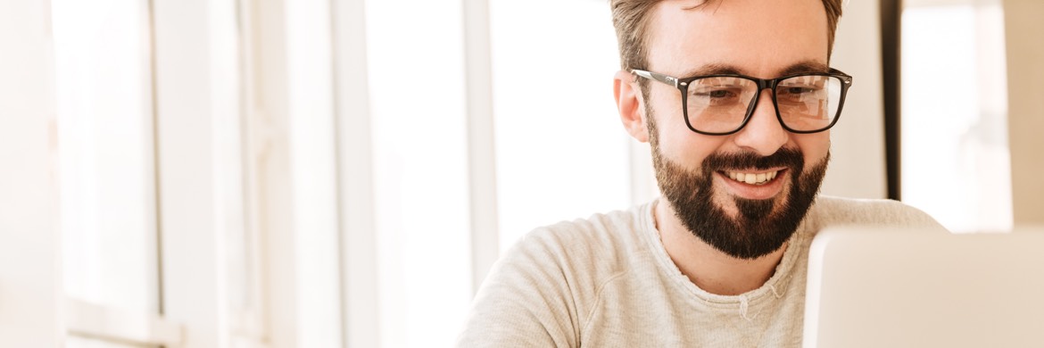 Ein Mann mit Brille und Bart schaut zufrieden lächelnd auf seinen Computer-Bildschirm